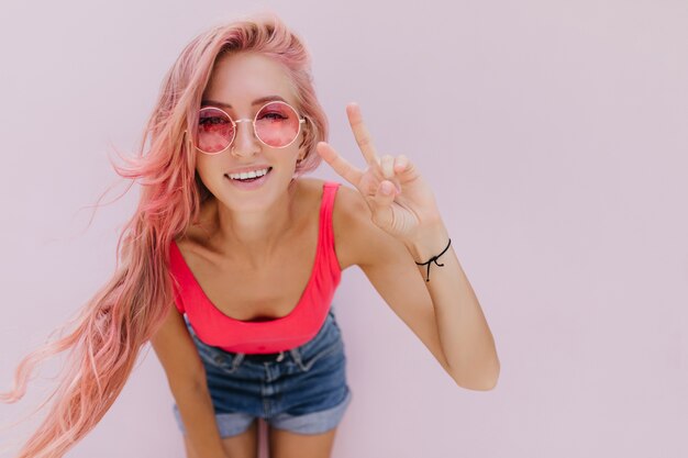 Alegre mujer caucásica con cabello rosado posando con linda sonrisa.