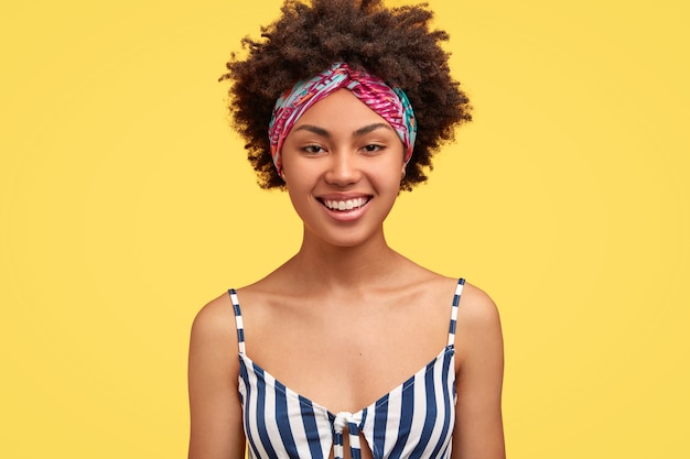 Alegre mujer encantadora con una gran sonrisa, vestida con camiseta a rayas, diadema, expresa positividad