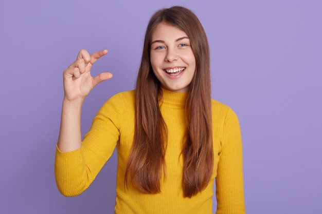 Alegre mujer joven con cabello largo y hermoso, muestra un tamaño muy pequeño con los dedos