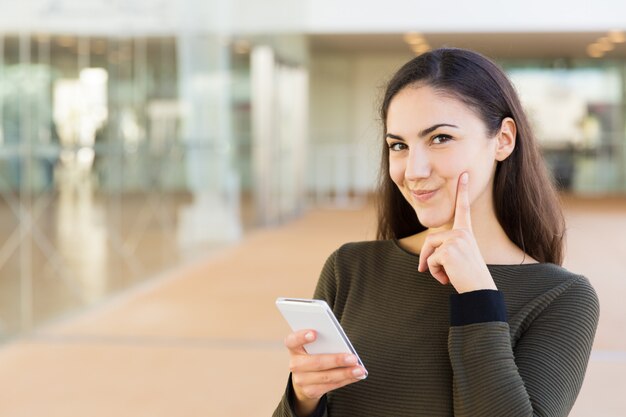 Alegre mujer latina pensativa con celular tocando la cara