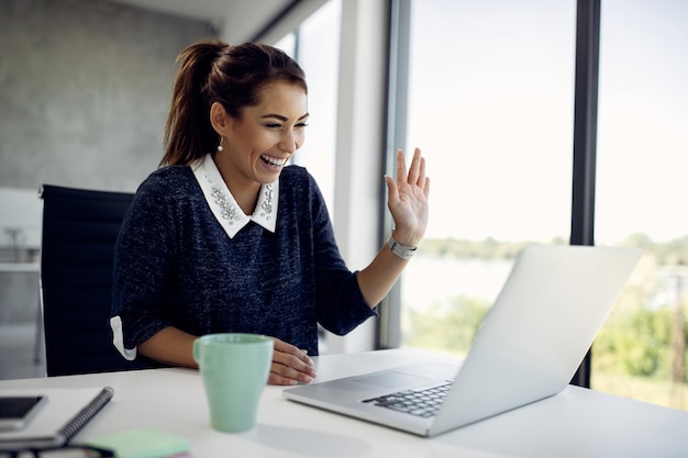 Alegre mujer de negocios saludando durante una videollamada en la oficina