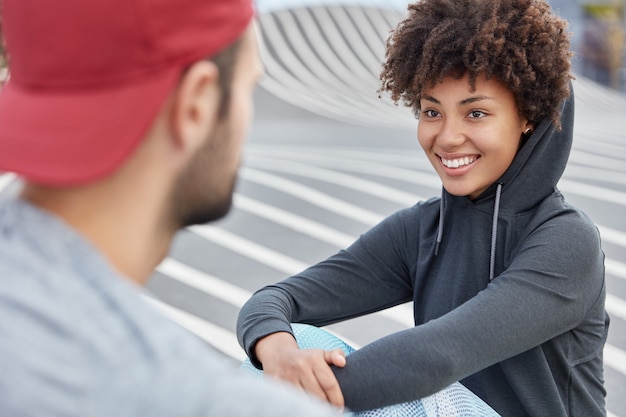 Alegre mujer negra en elegante sudadera mira deliciosamente al jugador de baloncesto masculino