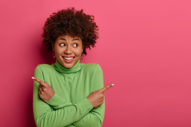 Alegre mujer de pelo rizado cruza los brazos sobre el pecho, señala a la izquierda y a la derecha, da dos variantes, dice que ambas son buenas, anuncia productos