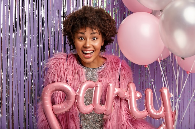 Foto gratuita alegre mujer de piel oscura rizada en abrigo rosa, lleva globos