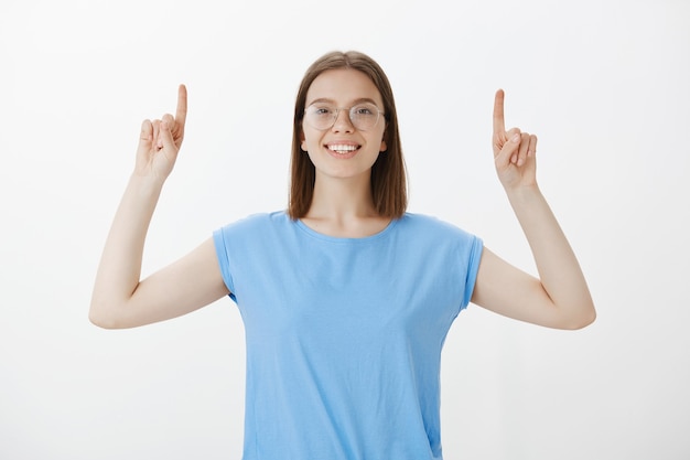 Alegre mujer sonriente apuntando con el dedo hacia arriba y mostrando publicidad