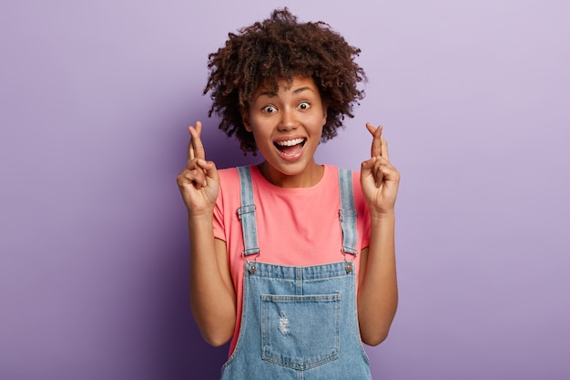 Alegre mujer sonriente desea suerte, siente emociones emocionadas, mantiene los dedos cruzados