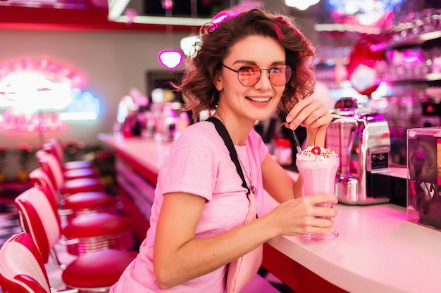 Alegre mujer sonriente muy elegante en colorido retro vintage american 50's cafe sentado en la mesa