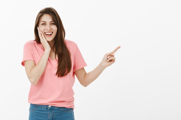 Alegre mujer sorprendida apuntando hacia la esquina superior derecha y sintiéndose feliz