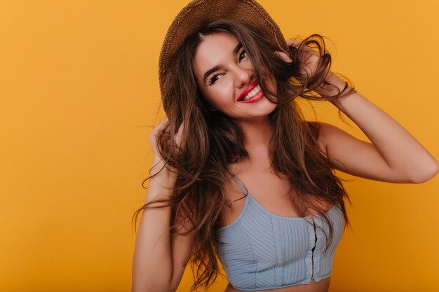 Alegre niña de cabello castaño con expresión de cara feliz jugando con su cabello y riendo