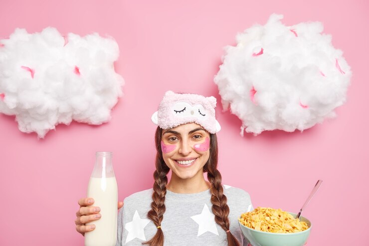 Foto gratuito alegre niña de cabello oscuro con coletas peinadas sostiene tazón de cereales y leche viste pijama