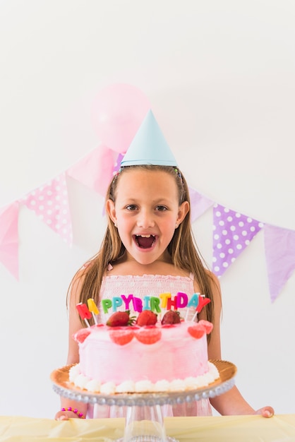 Alegre niña de cumpleaños sorprendida de pie detrás de pastel y velas