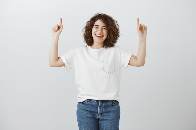 Alegre niña sonriente mostrando copyspace, sonriendo y señalando con el dedo hacia arriba