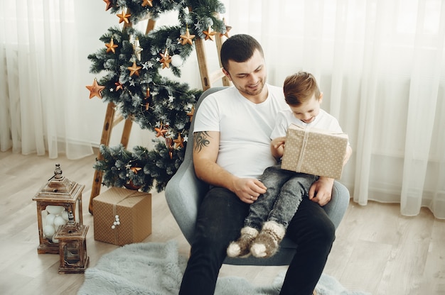 Alegre padre e hijo sentados cerca de decoraciones de Navidad. El niño está sentado con alegría