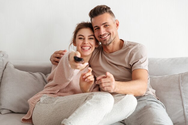 Alegre pareja amorosa sentados juntos en el sofá y viendo la televisión