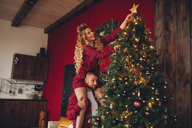 Alegre pareja de enamorados en la misma ropa de dormir decora el árbol de Navidad juntos en casa