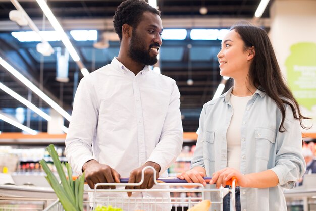 Alegre pareja multiétnica con carrito de compras en el supermercado