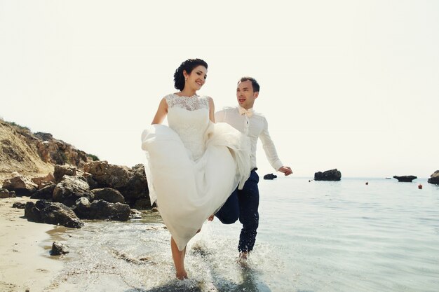 Alegre recién casados ​​correr a lo largo de la playa