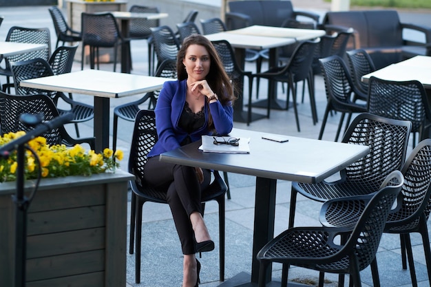 Una alegre y sonriente mujer de negocios está trabajando en sus documentos fuera de su oficina. Ella está sentada en un pequeño café.