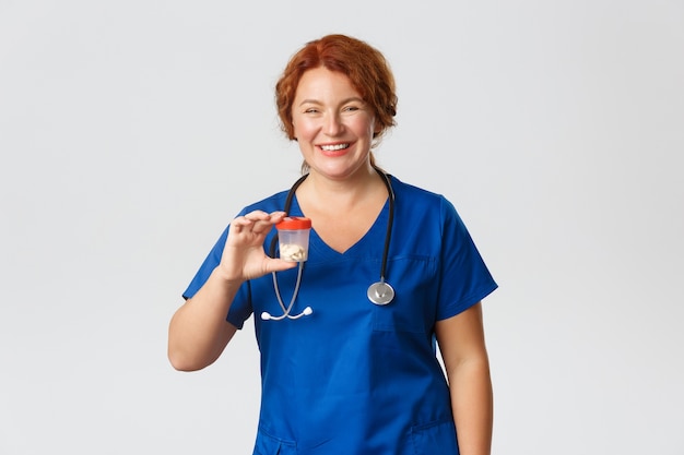 Alegre sonriente trabajadora meical, médico en matorrales mostrando el recipiente con vitaminas o medicamentos, recomendar pastillas, de pie