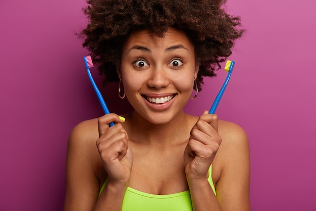 Alegre sorprendida mujer afroamericana tiene dos cepillos de dientes