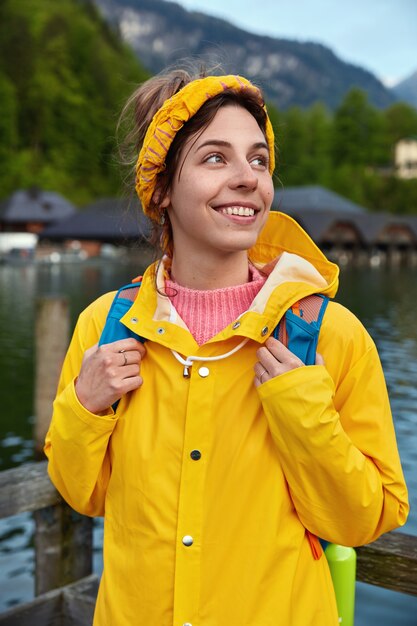 Alegre turista europea viaja en las montañas, posa cerca del lago, disfruta de un día cálido y soleado