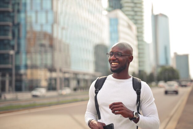 Alegre varón africano sonriente con gafas, vistiendo una camiseta blanca y una mochila al aire libre