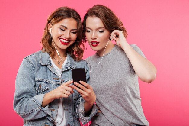 Alegres amigas usando teléfono móvil escuchando música.