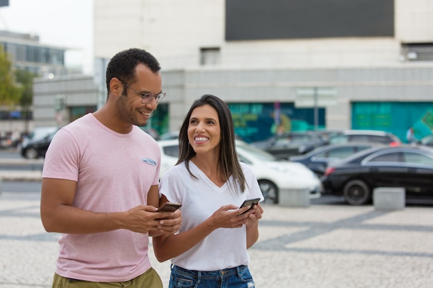 Alegres amigos paseando por la calle con teléfonos inteligentes