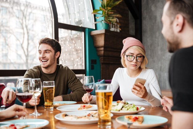 Alegres amigos sentados en la cafetería comiendo y bebiendo alcohol.