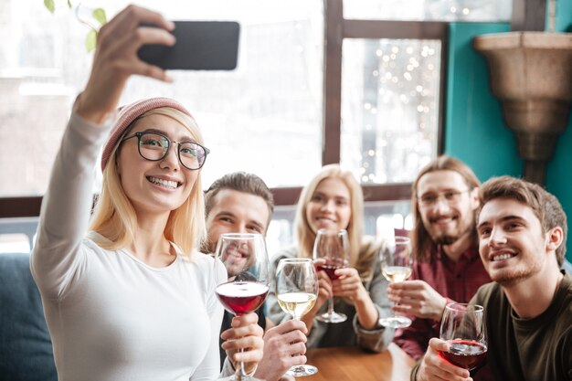 Alegres amigos sentados en la cafetería y hacen selfie por teléfono.