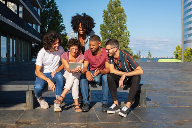 Alegres amigos viendo videos en tableta al aire libre