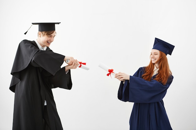 Alegres graduados sonrientes luchando con diplomas.