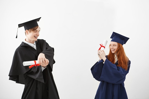 Alegres graduados sonrientes luchando con diplomas.