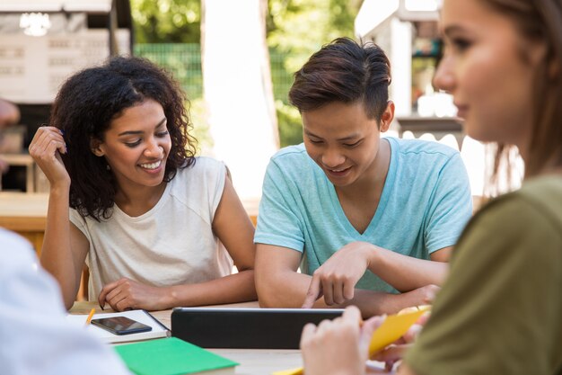 Alegres jóvenes amigos multiétnicos estudiantes al aire libre usando tableta