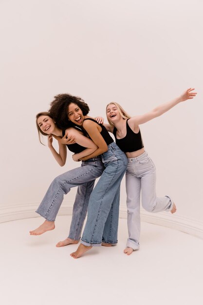 Alegres jóvenes caucásicas y africanas de longitud completa con ropa informal tonteando con fondo blanco