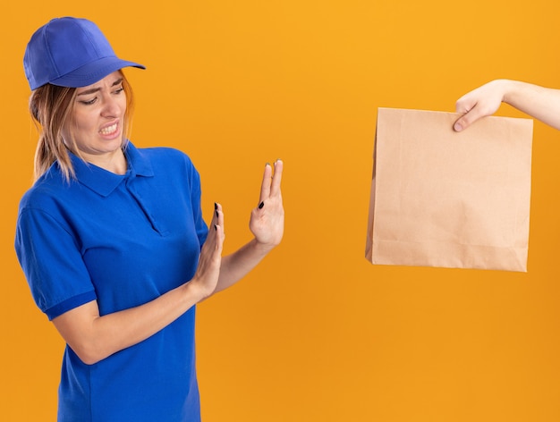 Alguien le da el paquete de papel a la joven y bonita repartidora disgustada en uniforme sin gesticular ninguna señal en naranja