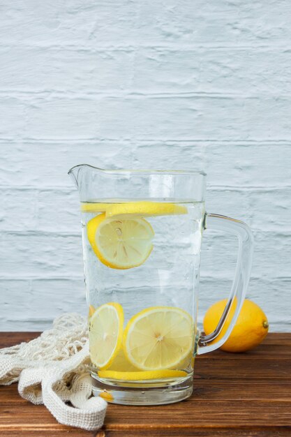 Foto gratuita alguna jarra de limón con limones sobre superficie de madera y blanca, vista lateral. espacio para texto