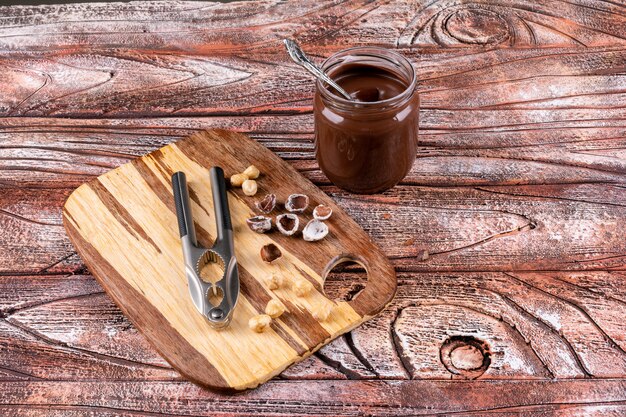 Algunas de las avellanas sin cáscara y limpias con crema de cacao y cascanueces en la mesa de madera, vista desde arriba.