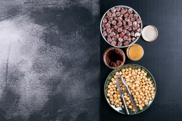 Foto gratuita algunas de las avellanas sin cáscara y limpias con crema de cacao y cascanueces en un recipiente blanco sobre la mesa de piedra oscura, vista desde arriba.