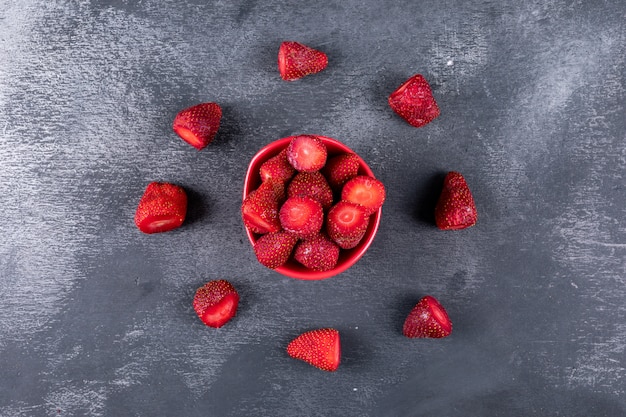 Foto gratuita algunas fresas con otras formando un círculo alrededor en un recipiente en la mesa oscura, vista desde arriba.