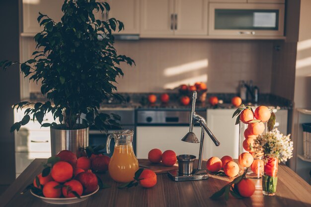 Algunas frutas con extractor de jugo y árbol en mesa y cocina, vista lateral.