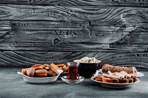 Algunas galletas con roulade, gofres en platos y tazón de madera oscura