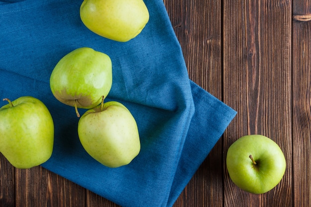 Algunas manzanas verdes en el paño azul y el fondo de madera, visión superior.