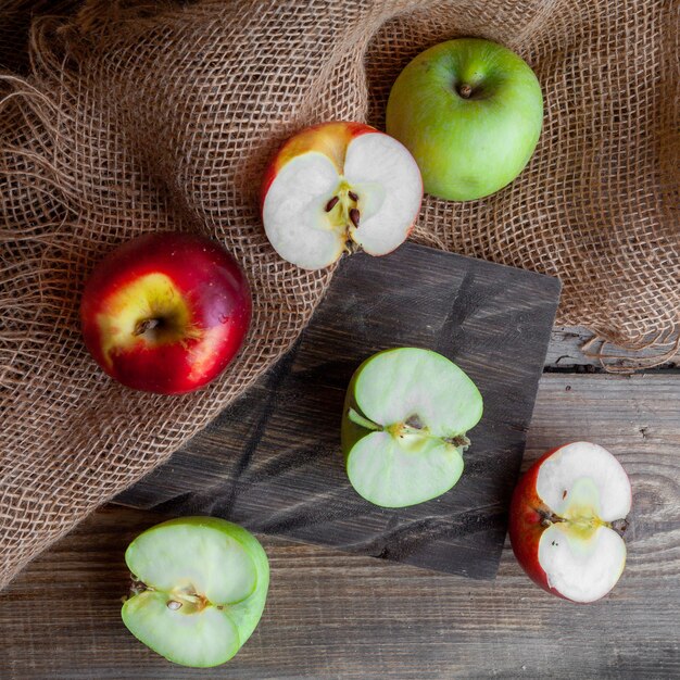 Algunas manzanas verdes y rojas cortan por la mitad en madera, tela y fondo de madera oscura, vista superior.