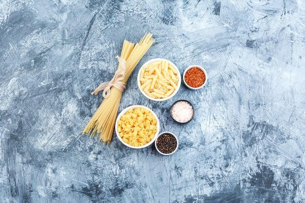 Algunas pastas variadas con especias en tazones sobre fondo de yeso gris, vista superior.