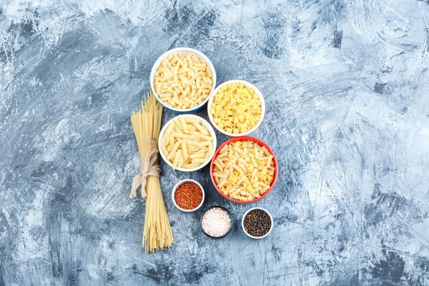 Algunas pastas variadas con especias en tazones sobre fondo de yeso gris, vista superior.