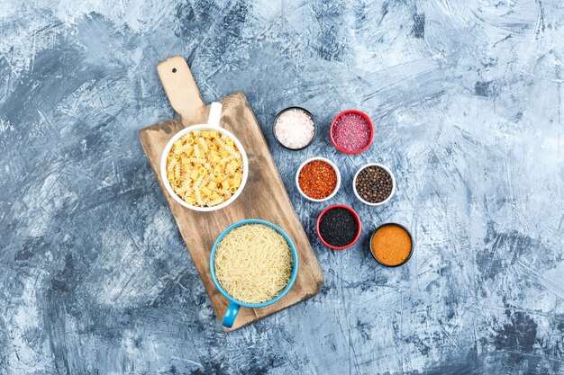 Algunas pastas variadas con especias en tazones sobre yeso gris y fondo de tabla de cortar, vista superior.