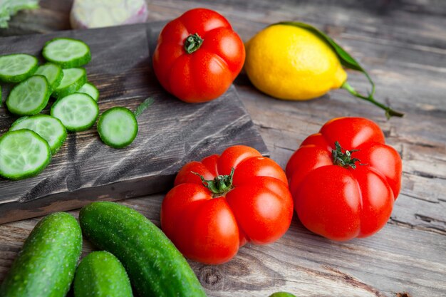 Algunas rodajas de pepino con ajo, tomate, limón en una tabla de cortar sobre fondo de madera oscura, vista de ángulo alto