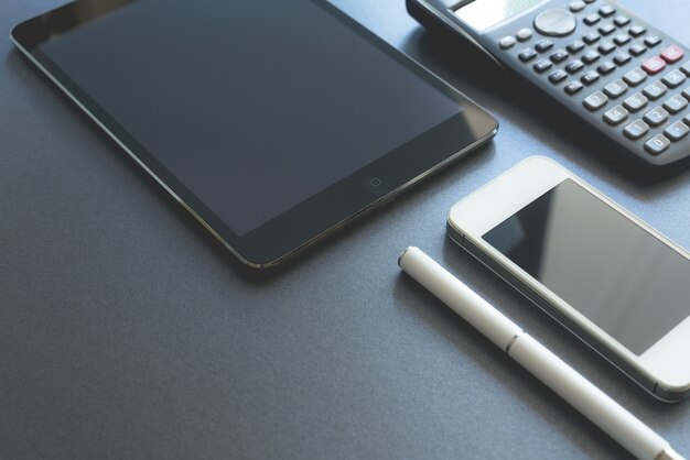 Algunos dispositivos electrónicos se muestran en fondo gris. Teléfono inteligente, pad y calculadora, todos digitales excepto un bolígrafo. Lugar de trabajo escena.