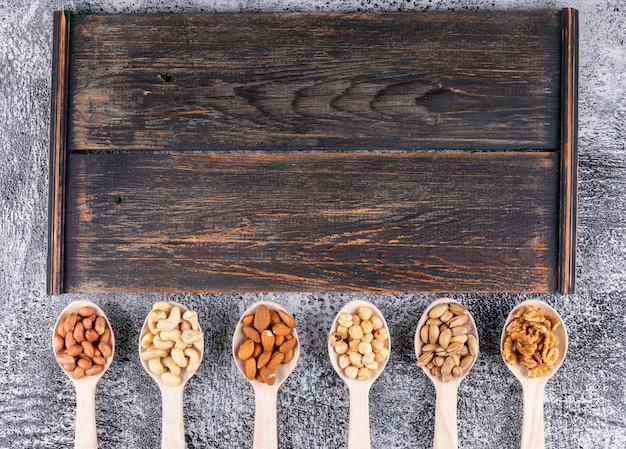 Algunos frutos secos variados y frutas secas con pacanas, pistachos, almendras, maní, en cucharas de madera sobre tabla de cortar de madera